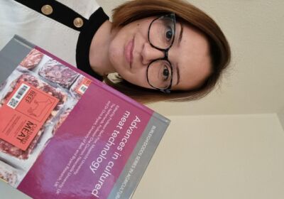 Petra Hanga smiling while holding a copy of the Advances in cultured meat technology book