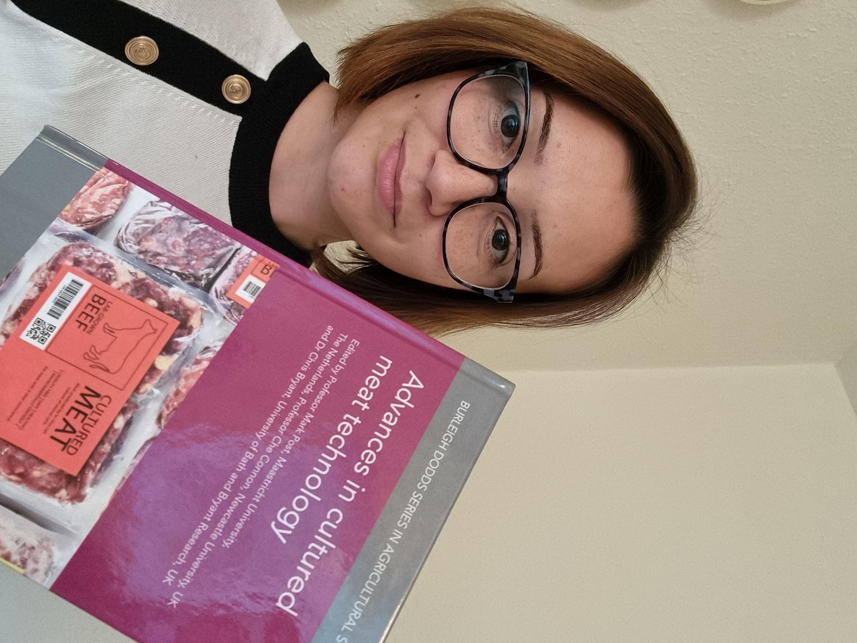 Petra Hanga smiling while holding a copy of the Advances in cultured meat technology book